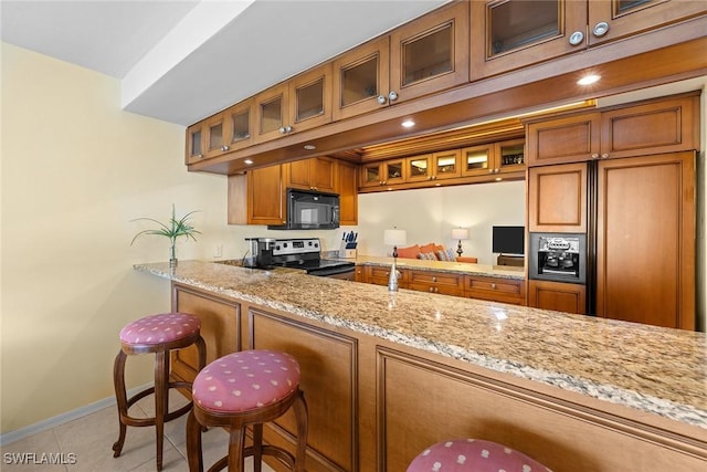 kitchen featuring light stone countertops, stainless steel electric stove, a breakfast bar area, and light tile patterned flooring