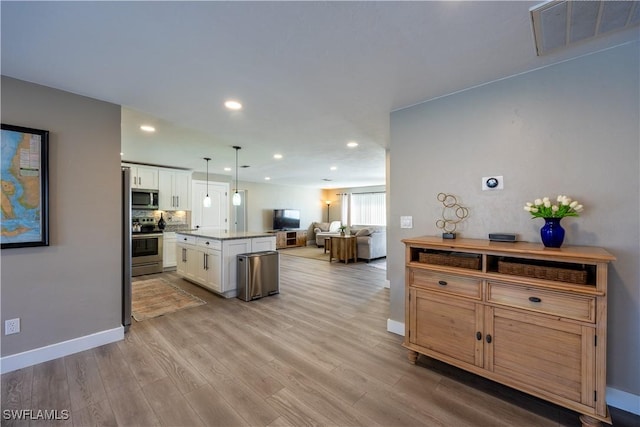 kitchen featuring appliances with stainless steel finishes, light wood-type flooring, white cabinets, a kitchen island, and hanging light fixtures