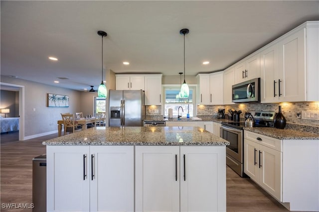 kitchen with decorative light fixtures, stainless steel appliances, a kitchen island, and sink