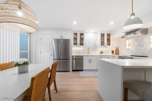 kitchen featuring backsplash, wall chimney exhaust hood, stainless steel appliances, pendant lighting, and white cabinets