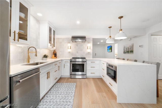 kitchen featuring appliances with stainless steel finishes, sink, wall chimney range hood, white cabinets, and hanging light fixtures