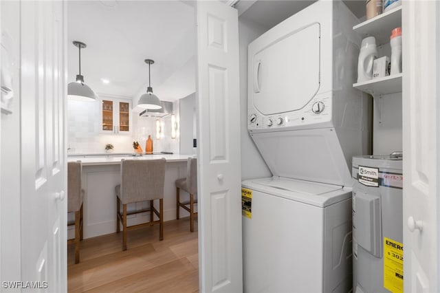 laundry room with electric water heater, light hardwood / wood-style floors, and stacked washing maching and dryer