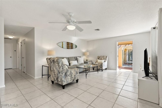 living area with light tile patterned floors, a ceiling fan, visible vents, and baseboards