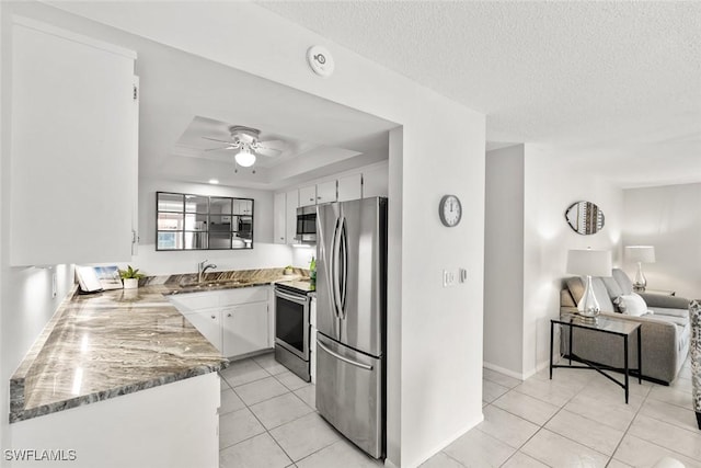 kitchen with stone countertops, a sink, appliances with stainless steel finishes, white cabinetry, and a raised ceiling