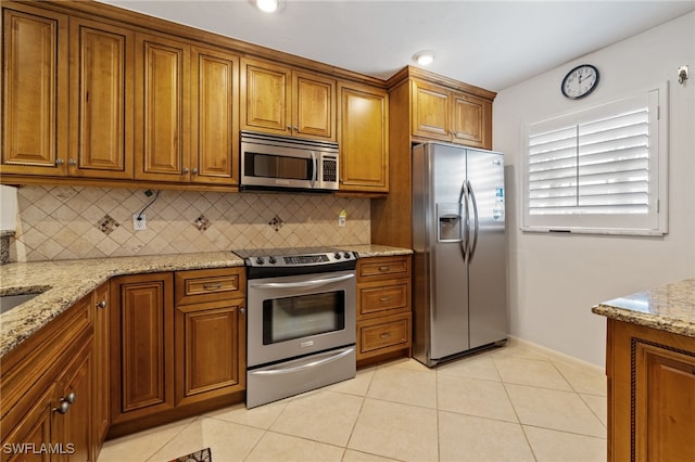 kitchen featuring light tile patterned floors, appliances with stainless steel finishes, backsplash, and light stone countertops