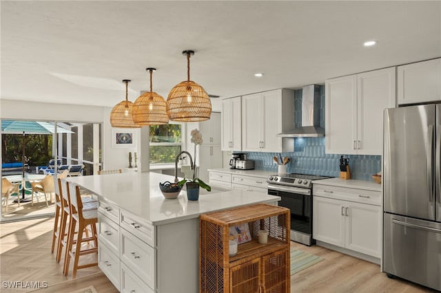 kitchen featuring a kitchen island with sink, wall chimney range hood, sink, white cabinetry, and stainless steel appliances