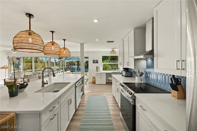 kitchen with pendant lighting, white cabinets, sink, wall chimney exhaust hood, and stainless steel appliances