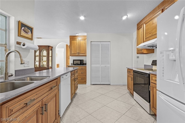 kitchen with a textured ceiling, white appliances, sink, and light tile patterned floors