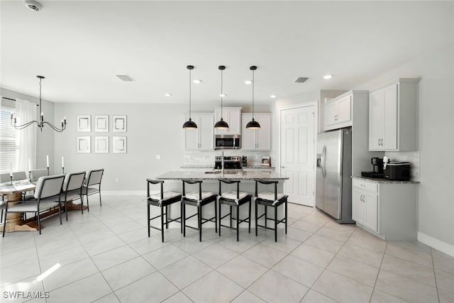 kitchen featuring a notable chandelier, light stone countertops, hanging light fixtures, a kitchen island with sink, and stainless steel appliances