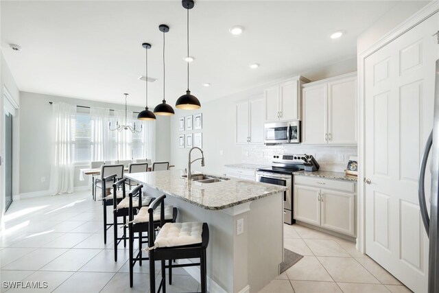 kitchen with white cabinetry, stainless steel appliances, an island with sink, sink, and hanging light fixtures