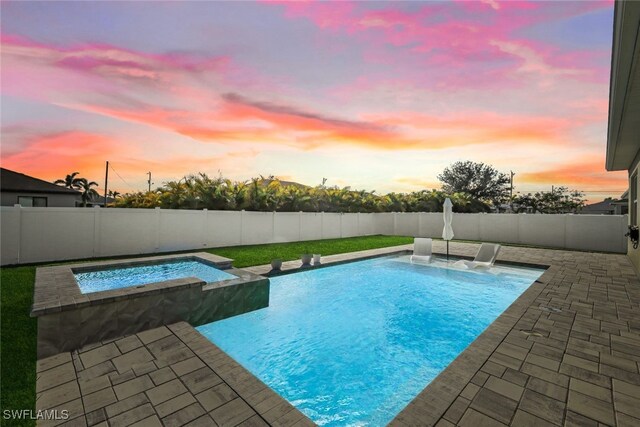 pool at dusk featuring pool water feature, an in ground hot tub, and a patio