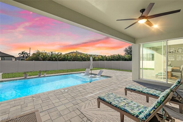 pool at dusk with ceiling fan and a patio area