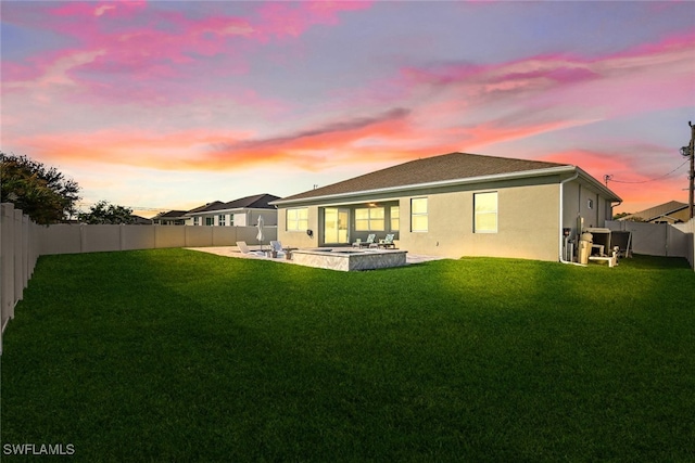 back house at dusk featuring a patio and a yard