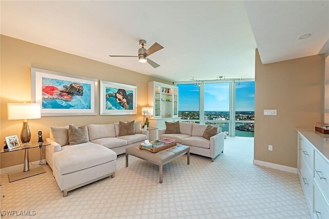 living room featuring ceiling fan, light colored carpet, baseboards, and expansive windows