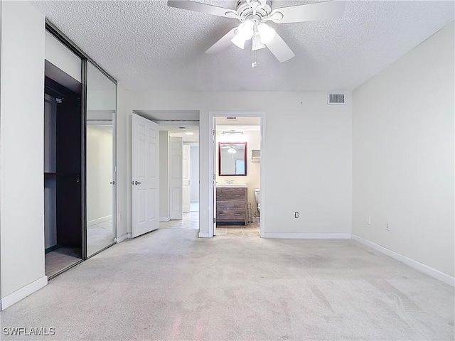 unfurnished bedroom featuring ensuite bathroom, light carpet, ceiling fan, and a textured ceiling