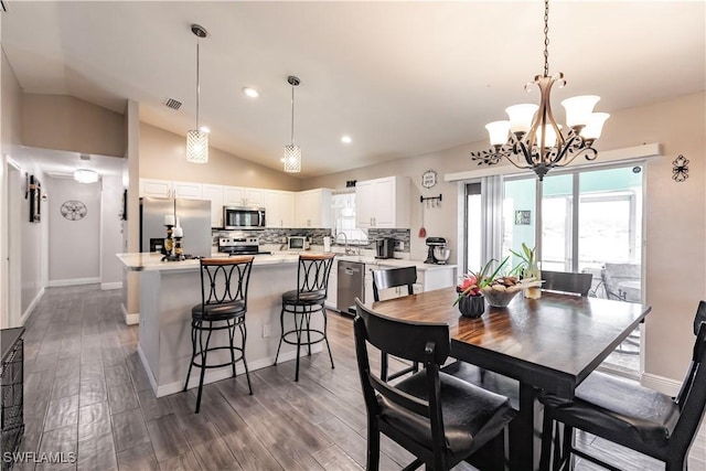 dining room with an inviting chandelier, sink, dark wood-type flooring, and vaulted ceiling