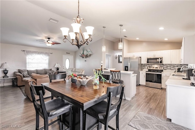 dining area with ceiling fan, lofted ceiling, sink, and light wood-type flooring