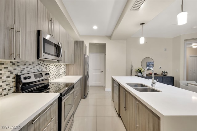 kitchen featuring backsplash, a center island with sink, sink, hanging light fixtures, and appliances with stainless steel finishes