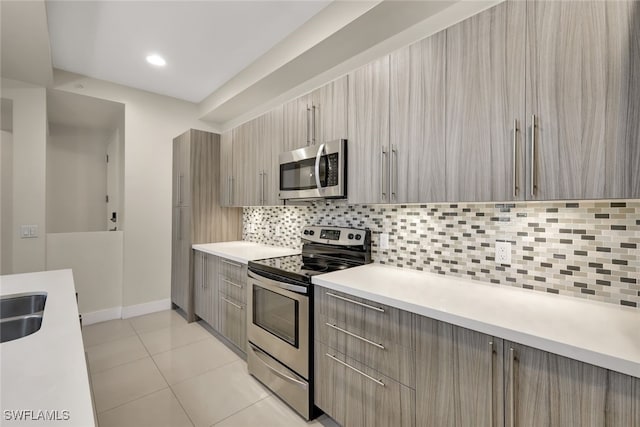 kitchen with decorative backsplash, appliances with stainless steel finishes, light brown cabinetry, sink, and light tile patterned floors