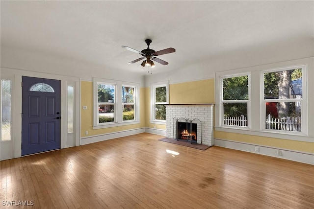 unfurnished living room with light hardwood / wood-style flooring, a brick fireplace, ceiling fan, and plenty of natural light