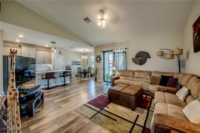 living room with vaulted ceiling, ceiling fan with notable chandelier, and light wood-type flooring