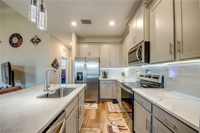 kitchen featuring sink, decorative backsplash, decorative light fixtures, light hardwood / wood-style floors, and stainless steel appliances