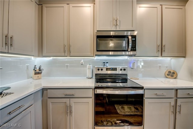 kitchen featuring gray cabinetry, decorative backsplash, light stone counters, and appliances with stainless steel finishes