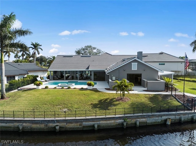 back of property with a lawn, a patio area, a water view, and a fenced in pool