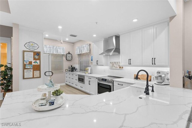 kitchen with white cabinets, light stone counters, wall chimney range hood, and stainless steel appliances