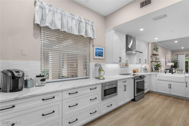 790 W Elkcam Cir Unit 103, Marco Island, FL 34145 - kitchen featuring visible vents, wall chimney range hood, white cabinets, tasteful backsplash, and appliances with stainless steel finishes