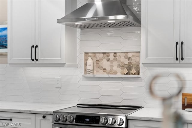 kitchen with decorative backsplash, stainless steel range, white cabinets, and wall chimney range hood