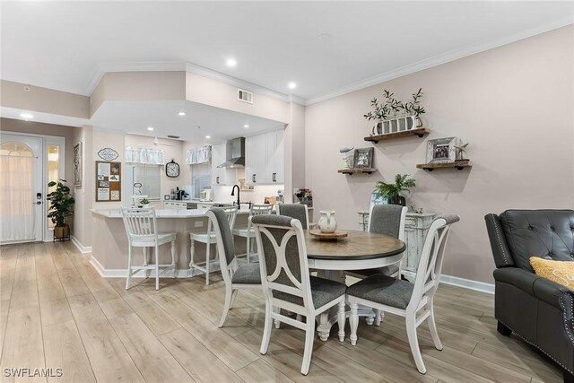 dining room featuring sink, crown molding, and light hardwood / wood-style floors