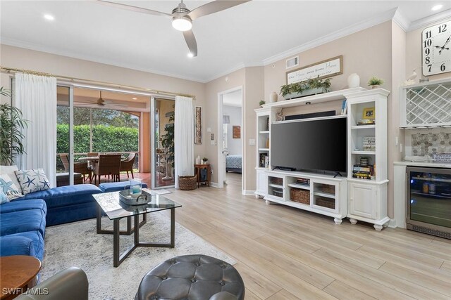 living room with beverage cooler, crown molding, bar, and light hardwood / wood-style flooring