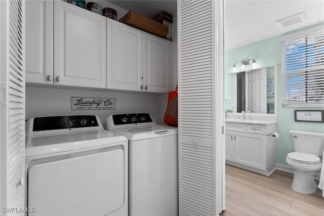 laundry room featuring cabinets, sink, washer and dryer, and light hardwood / wood-style flooring