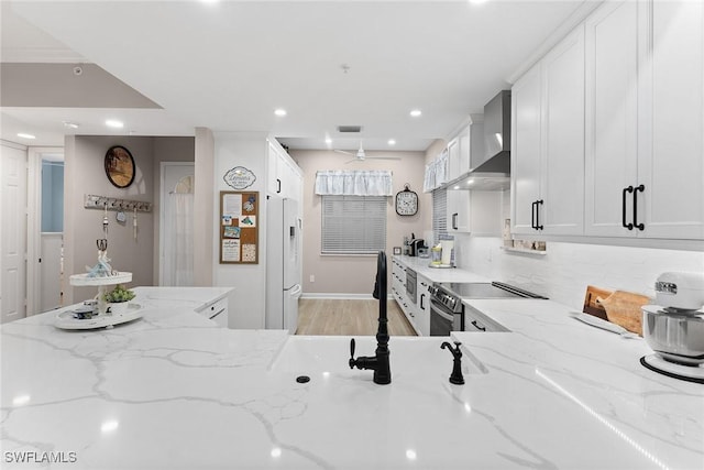 kitchen featuring white cabinetry, white fridge with ice dispenser, wall chimney range hood, light stone counters, and stainless steel electric range