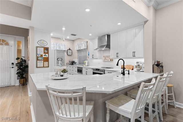 kitchen with a kitchen bar, white cabinetry, light stone counters, and wall chimney range hood