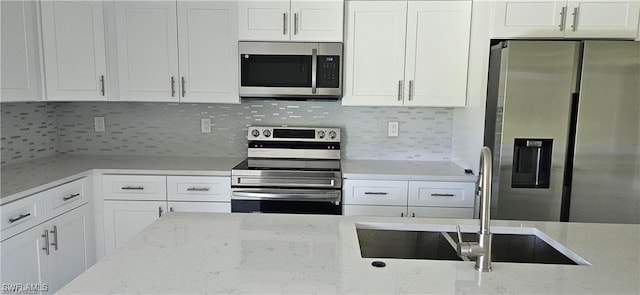 kitchen with appliances with stainless steel finishes, tasteful backsplash, white cabinets, sink, and light stone counters