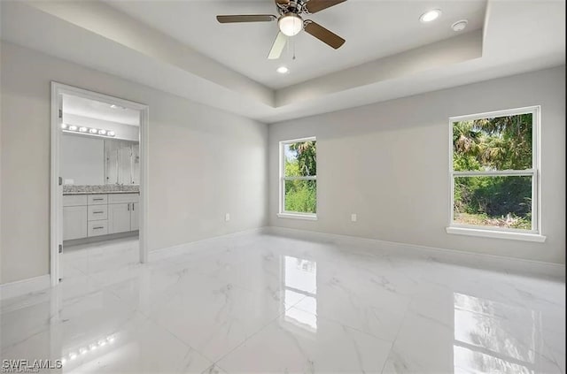 unfurnished bedroom with ceiling fan, ensuite bath, and a raised ceiling