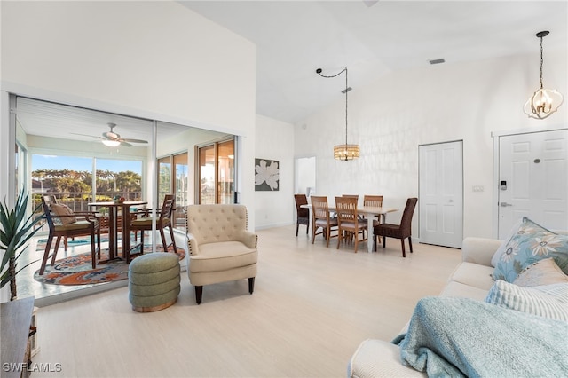 living room featuring high vaulted ceiling, ceiling fan with notable chandelier, and light wood-type flooring