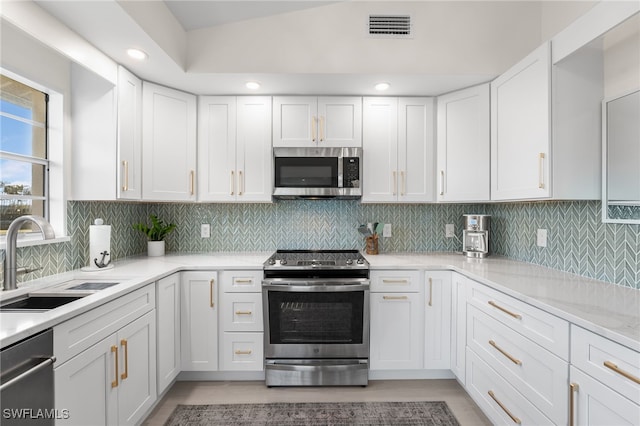 kitchen with light stone countertops, sink, tasteful backsplash, white cabinets, and appliances with stainless steel finishes