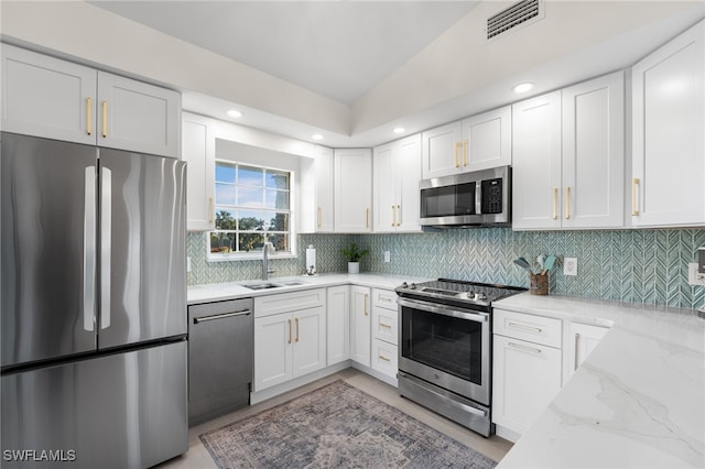 kitchen featuring sink, light stone counters, decorative backsplash, white cabinets, and appliances with stainless steel finishes