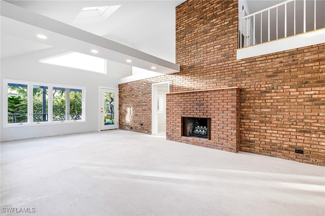 unfurnished living room featuring vaulted ceiling with skylight, brick wall, and a brick fireplace