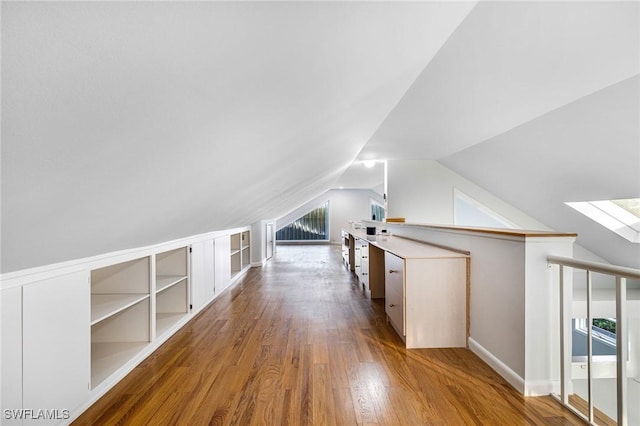 additional living space featuring lofted ceiling with skylight, built in features, and hardwood / wood-style flooring