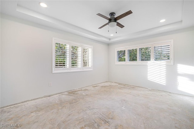 empty room featuring a raised ceiling, ceiling fan, and plenty of natural light