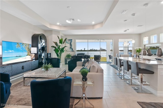 living room featuring light tile patterned flooring, sink, a raised ceiling, and a chandelier