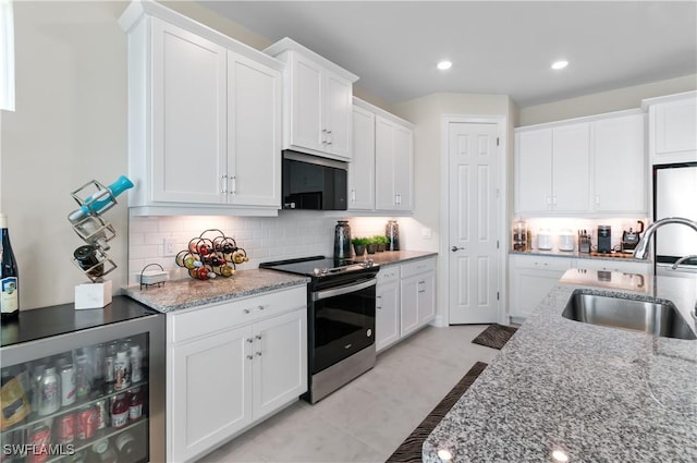 kitchen featuring black microwave, beverage cooler, stainless steel range with electric stovetop, white cabinetry, and a sink