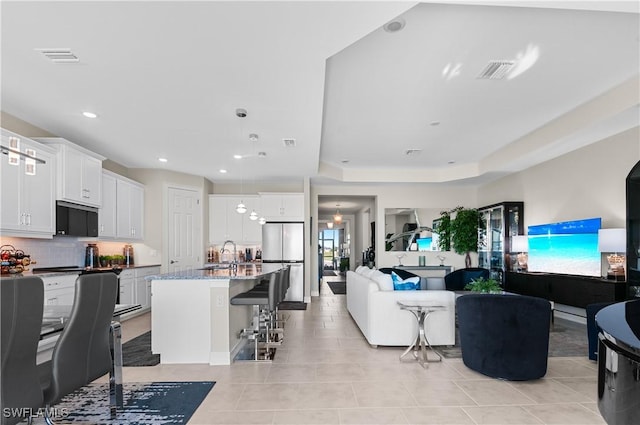 living room with a raised ceiling, light tile patterned flooring, and sink