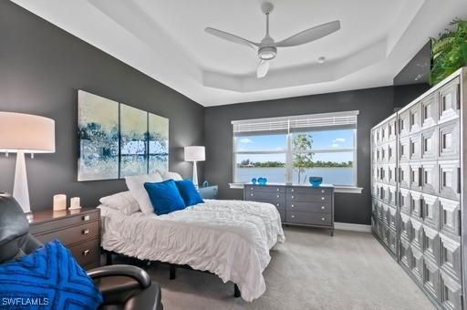 bedroom with light carpet, a raised ceiling, ceiling fan, and a water view