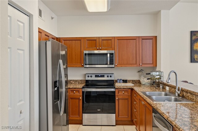 kitchen with stone counters, appliances with stainless steel finishes, light tile patterned floors, and sink