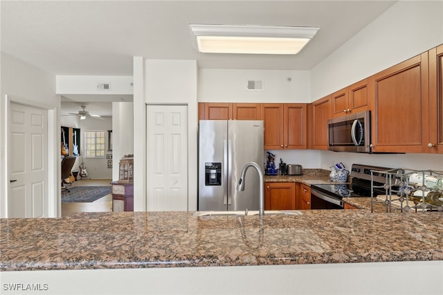 kitchen featuring stainless steel appliances, ceiling fan, dark stone counters, and sink